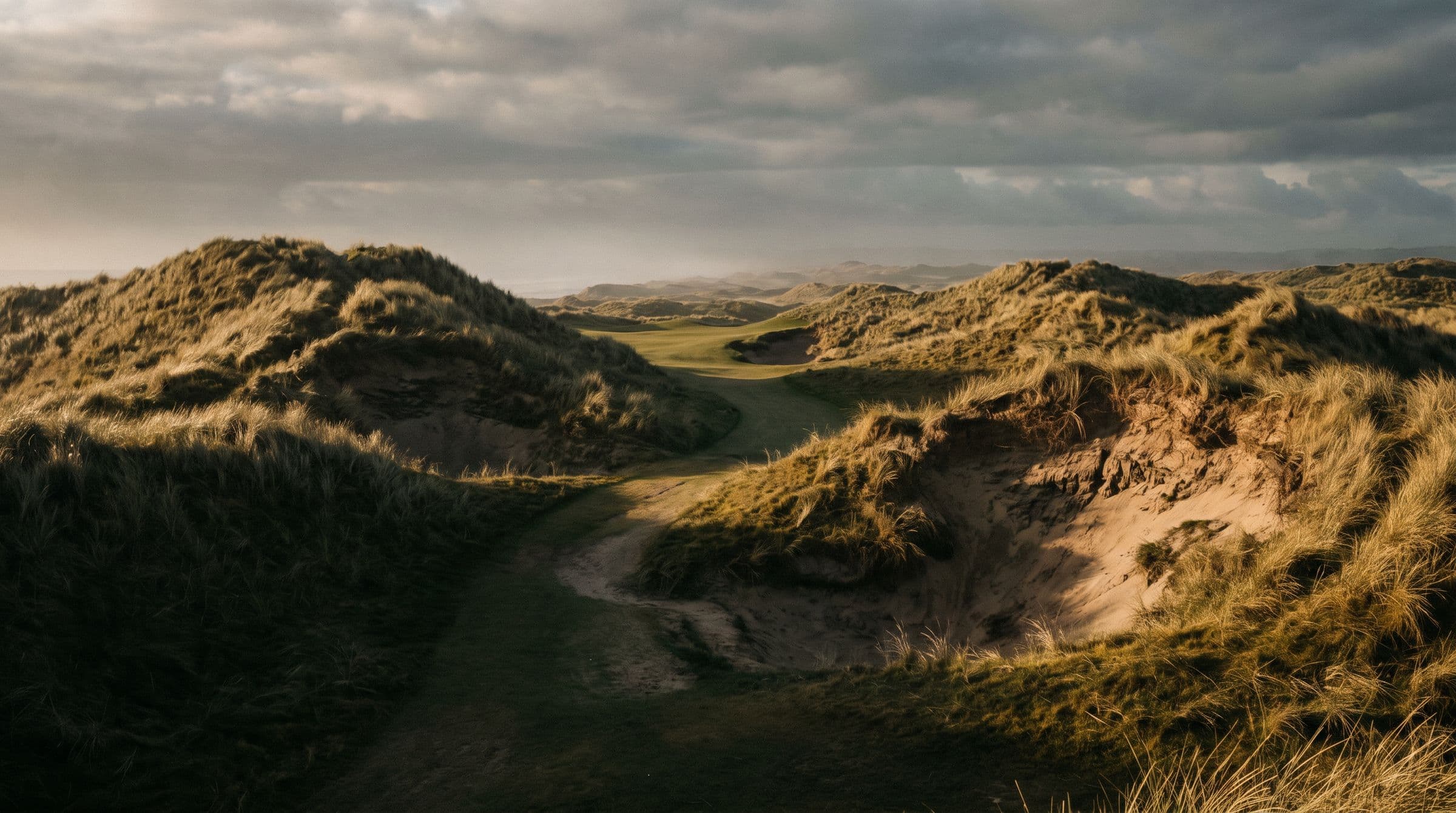 A narrow fairway running between tall marram-covered dunes with pot bunkers cut into their faces.